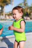A baby is standing side face to the camera in front of a pool wearing a key lime green Infant Warm Belly Wetsuit.