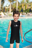 A smiling little boy is standing next to a pool wearing a children's Warm Belly Wetsuit in black.